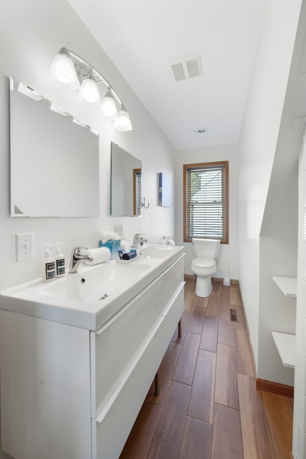 Modern bathroom featuring a double sink vanity, bright lighting, and natural wood flooring.