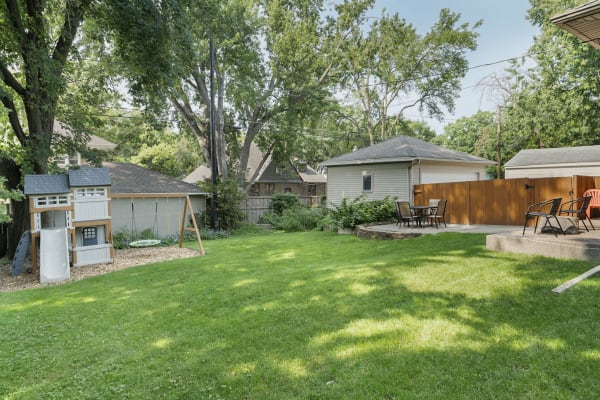 A spacious backyard with a playhouse, swings, and a comfortable seating area.