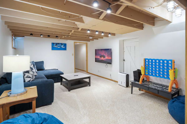 A cozy basement living area featuring a sectional sofa, coffee table, and large TV with playful game set.