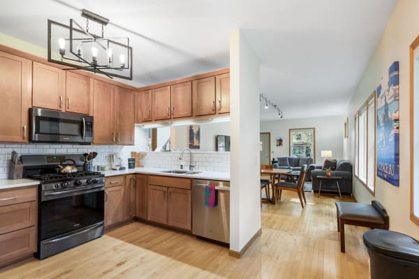 Modern kitchen with wooden cabinets and stainless steel appliances, leading to a cozy living area.