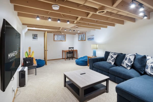 A stylish basement living room featuring a navy blue sectional sofa, blue bean bags, and a wooden table.