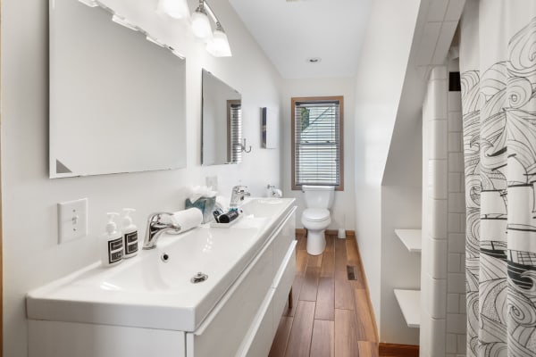 A modern bathroom featuring a double vanity, wooden flooring, and natural light from a window.