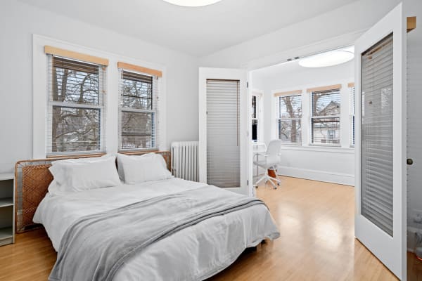 A cozy bedroom featuring a woven headboard bed, large windows, and a study area.