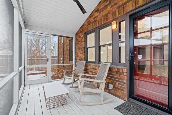 A screened-in porch featuring two rocking chairs and a small coffee table, with a view of the snowy outdoors.