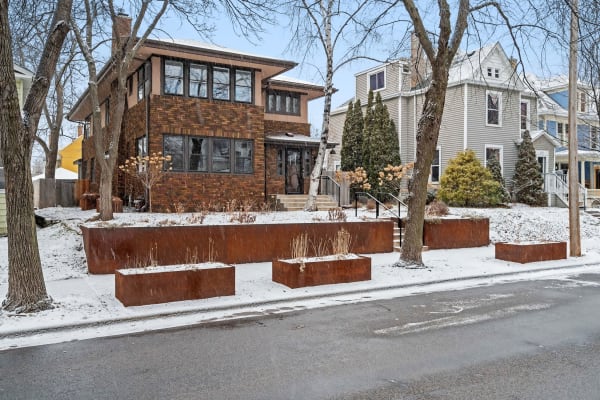 Winter scene of a brick house with snow-covered landscape and decorative planters.