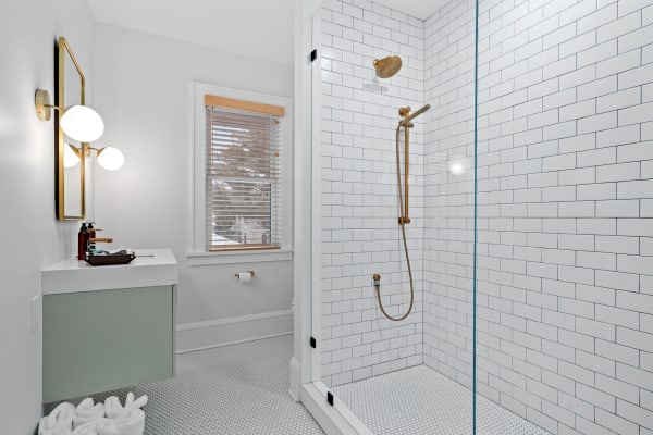 Modern bathroom featuring a glass-enclosed shower, golden fixtures, and a soft green sink cabinet.