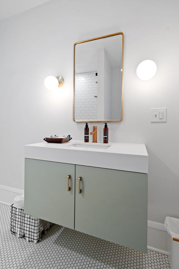 Modern bathroom vanity with white countertop, green cabinets, and warm light fixtures.