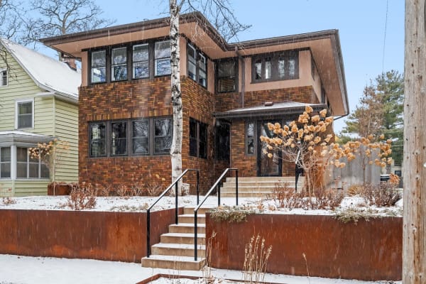 A modern brown brick house in winter, surrounded by snow and sparse plants.