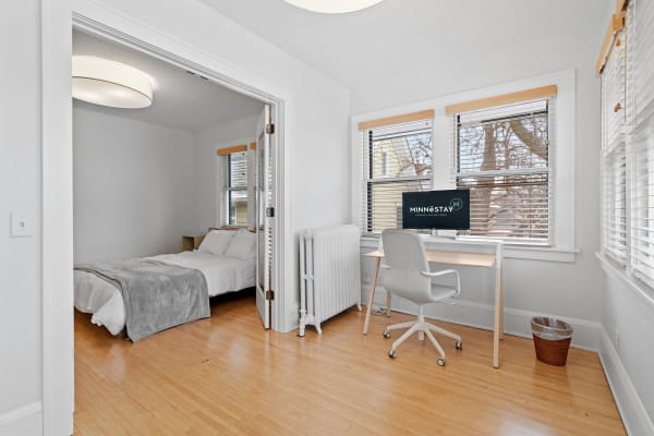 A bright bedroom with a double bed, desk, and computer monitor.