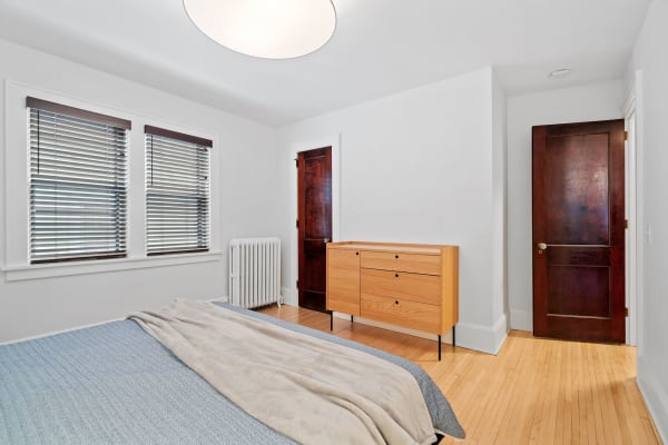 Minimalist bedroom with wooden dresser, soft bedding, and natural light through windows.