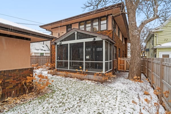 A residential backyard with a screened porch covered lightly in snow.