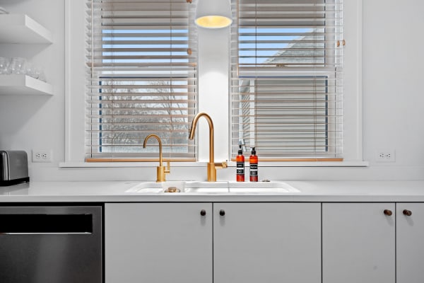 Modern kitchen showcasing a double sink with gold faucet, wooden blinds, and two decorative bottles.