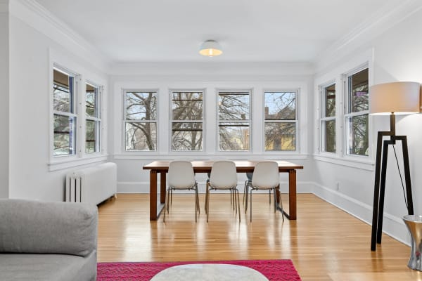 Bright dining area with wooden table and white chairs near large windows.