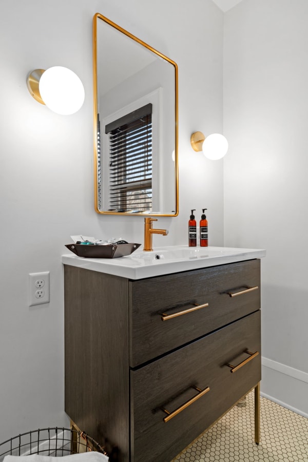 A contemporary bathroom featuring a dark wood vanity, white countertop, gold-framed mirror, and decorative lighting.