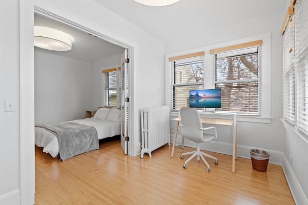 A view of a modern bedroom featuring a bed, desk with computer monitor, and large windows.