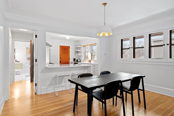 Bright and modern dining area with a wooden table and black chairs, leading into a kitchen.