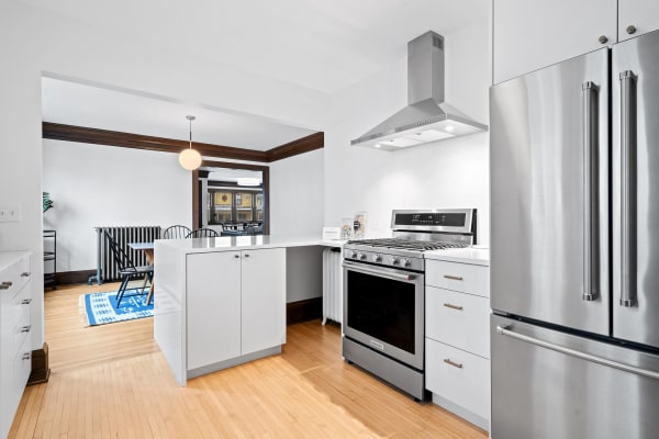 Modern kitchen with white cabinets and stainless steel appliances, featuring a dining area in the background.