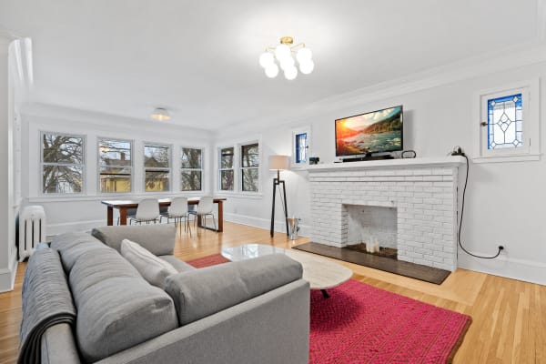 A bright living room with a gray sofa, white brick fireplace, and dining area.