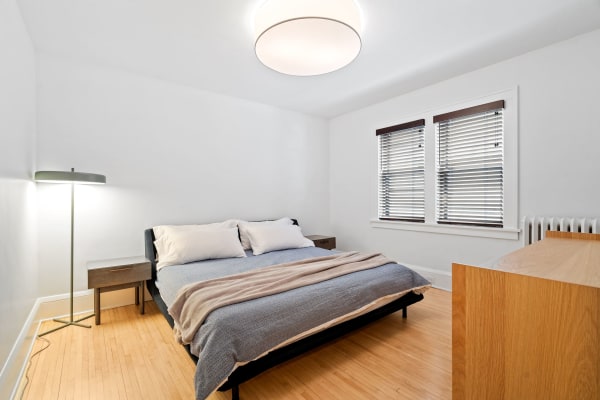 A minimalistic bedroom with a bed, nightstand, floor lamp, and wooden accents.