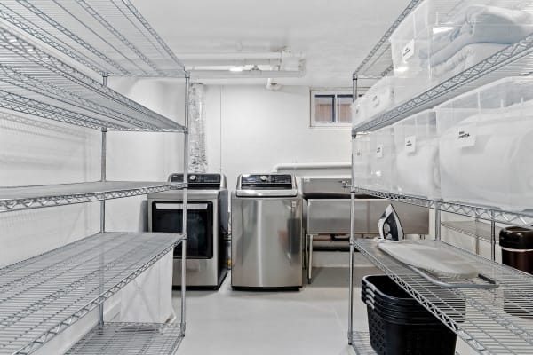 A clean laundry room with metallic shelves, washing machines, and labeled storage bins.