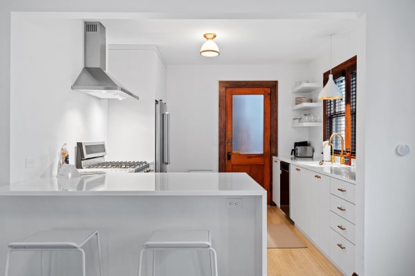 Contemporary kitchen featuring white cabinetry, stainless steel appliances, and wooden door.