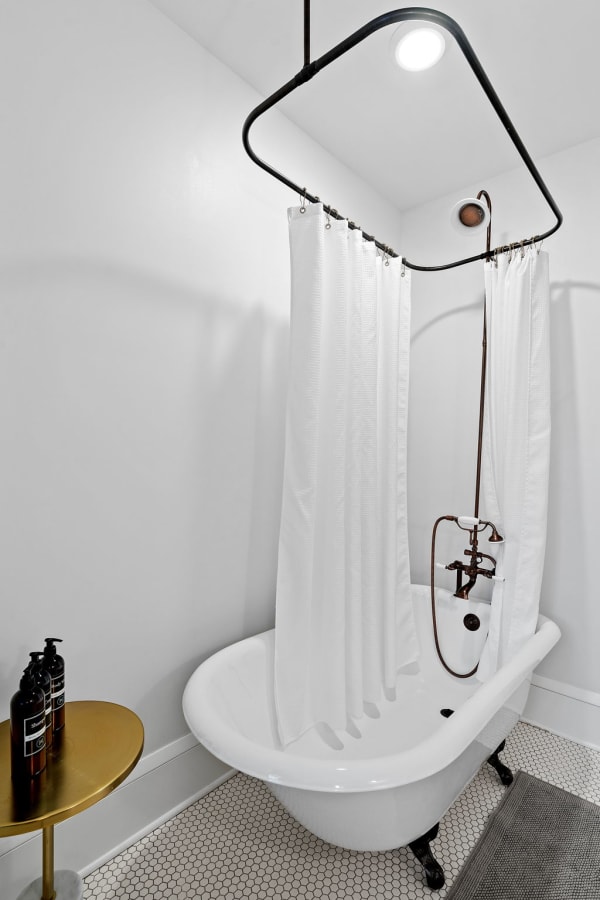 Chic bathroom featuring a clawfoot bathtub, black metal shower frame, and gold side table with shampoo.