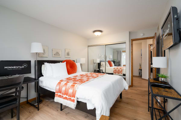 Modern bedroom with a bed, desk, and a TV, featuring bright accents and a mirror.
