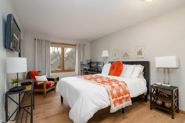 Bright and inviting bedroom featuring a king-sized bed with orange accents, a reading nook, and a desk setup.