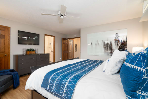 Modern bedroom featuring a blue quilted bedspread and a mounted TV.