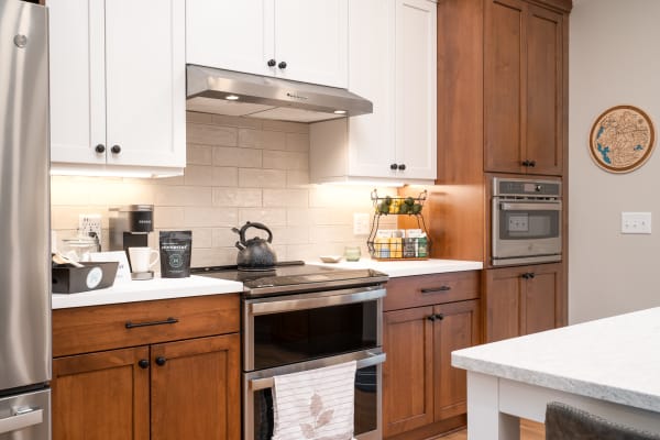 Modern kitchen with white upper cabinets and dark wood lower cabinets, stainless steel appliances, and a black stove.