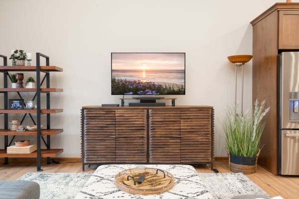 Cozy living room featuring a wooden TV stand, an open shelving unit, and a scenic sunset on the TV.