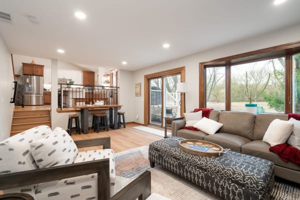 An inviting living room featuring a gray leather sofa, an ottoman, and a view of the kitchen and outdoors.