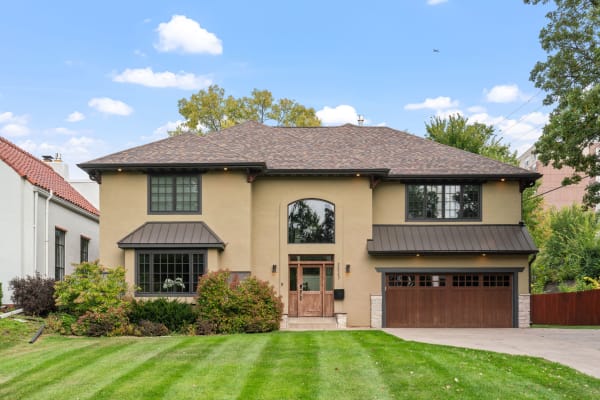 A contemporary two-story home with beige stucco, dark accents, and a lush green lawn.