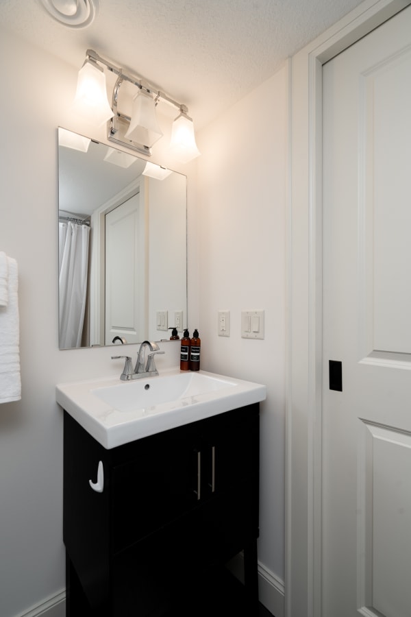 A modern bathroom featuring a white countertop sink on a dark vanity, illuminated by stylish light fixtures.