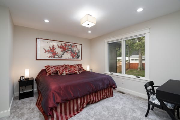 A modern bedroom featuring a plush red bed, decorative pillows, and a large window.