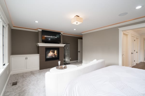 Cozy modern bedroom featuring a white bed, curved sofa, fireplace, and TV.