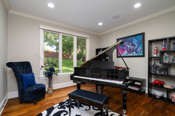 A grand piano in a music room surrounded by large windows and decorative items.