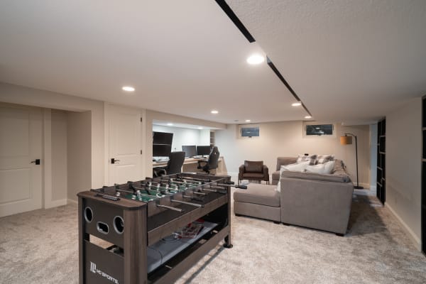 Modern basement room with foosball table, sectional sofa, and office setup.