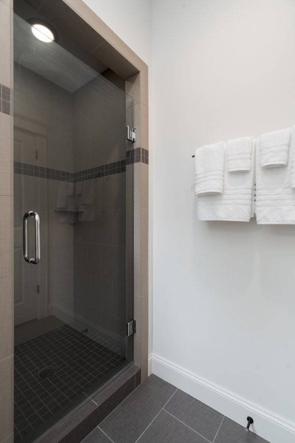 A stylish bathroom with a glass shower, gray tiles, and white towels.