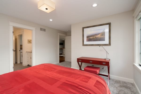 A contemporary bedroom featuring a red bedspread, a stylish red desk, and a coastal landscape photograph on the wall.
