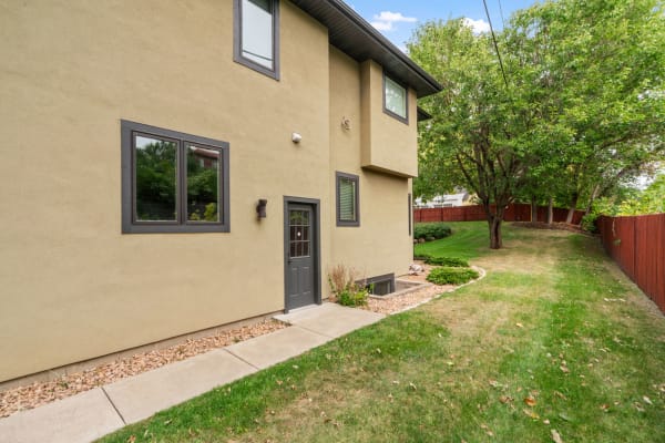 A modern two-story house with tan stucco exterior and dark trim, featuring a concrete pathway and green lawn.