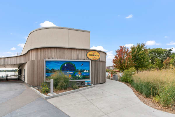 Modern building with a curved design and colorful mural, surrounded by trees and a lake.