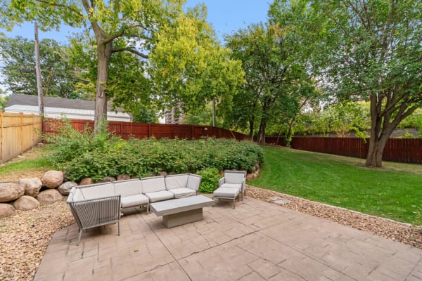 Backyard patio with a modern sectional sofa, coffee table, greenery, and wooden fence.