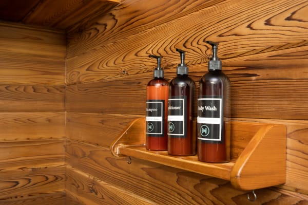 Three bottles of shampoo, conditioner, and body wash on a wooden shelf against a wooden wall.