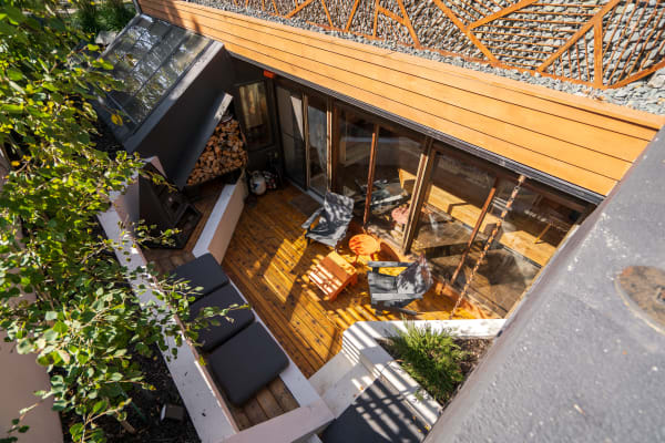 An aerial view of a stylish outdoor space featuring wooden decking, modern furniture, and a slanted glass roof.