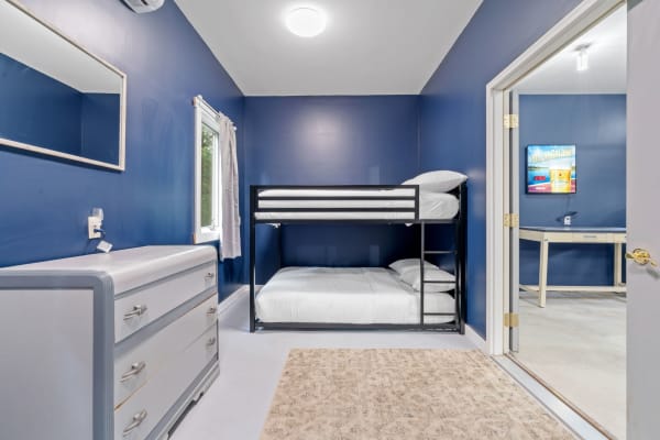 A modern bedroom featuring blue walls, a black bunk bed, a silver dresser, and a small window.