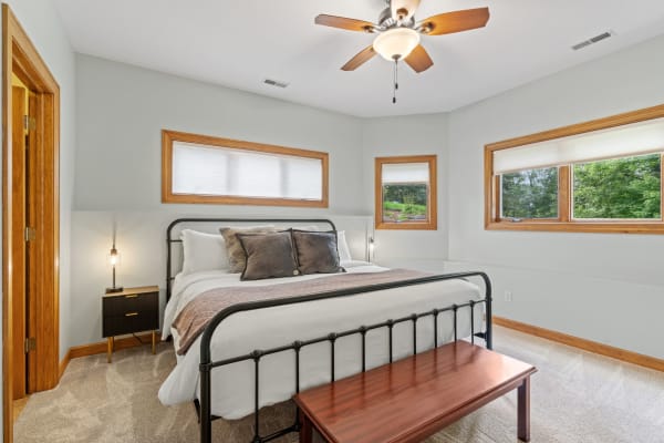 Modern bedroom design with black metal bed frame, decorative pillows, and natural light from windows.