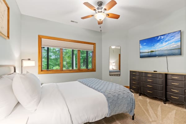 Cozy bedroom featuring a neatly made bed, large windows with greenery view, and modern decor.
