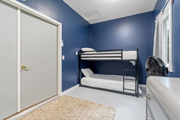Cozy bedroom featuring a black bunk bed, navy walls, and a window with curtains.