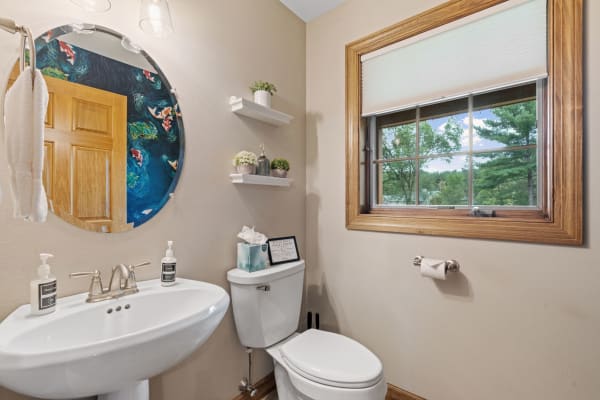 Modern bathroom featuring a round mirror, white sink, and greenery.